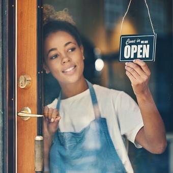 Shot of a young woman hanging an open sign on the window of a cafe